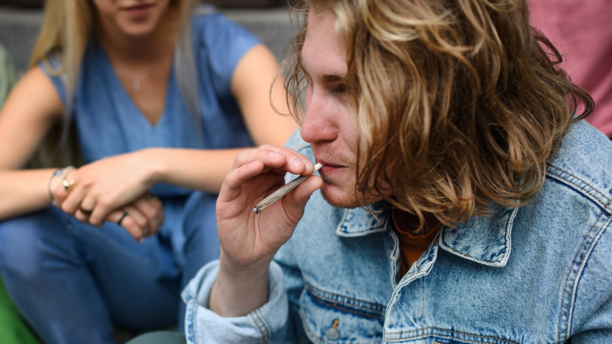 Young teenager smoking marihuana joint. Social problems, addiction concept. Wide photography.