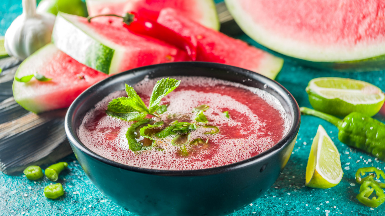 Summer cold watermelon smoothie gazpacho soup, marine blue background with watermelon slices, lime and herbs