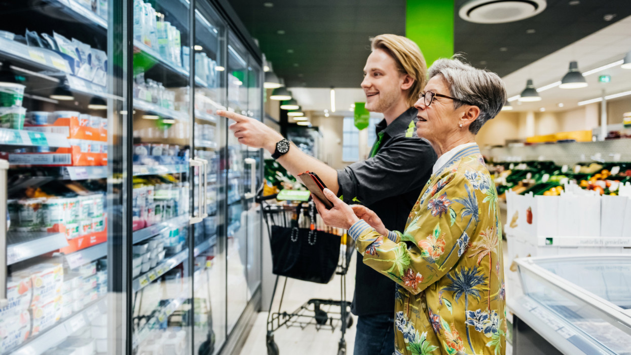 A grocery store clerk helping a senior woman with a question about a food item in her local supermarket.