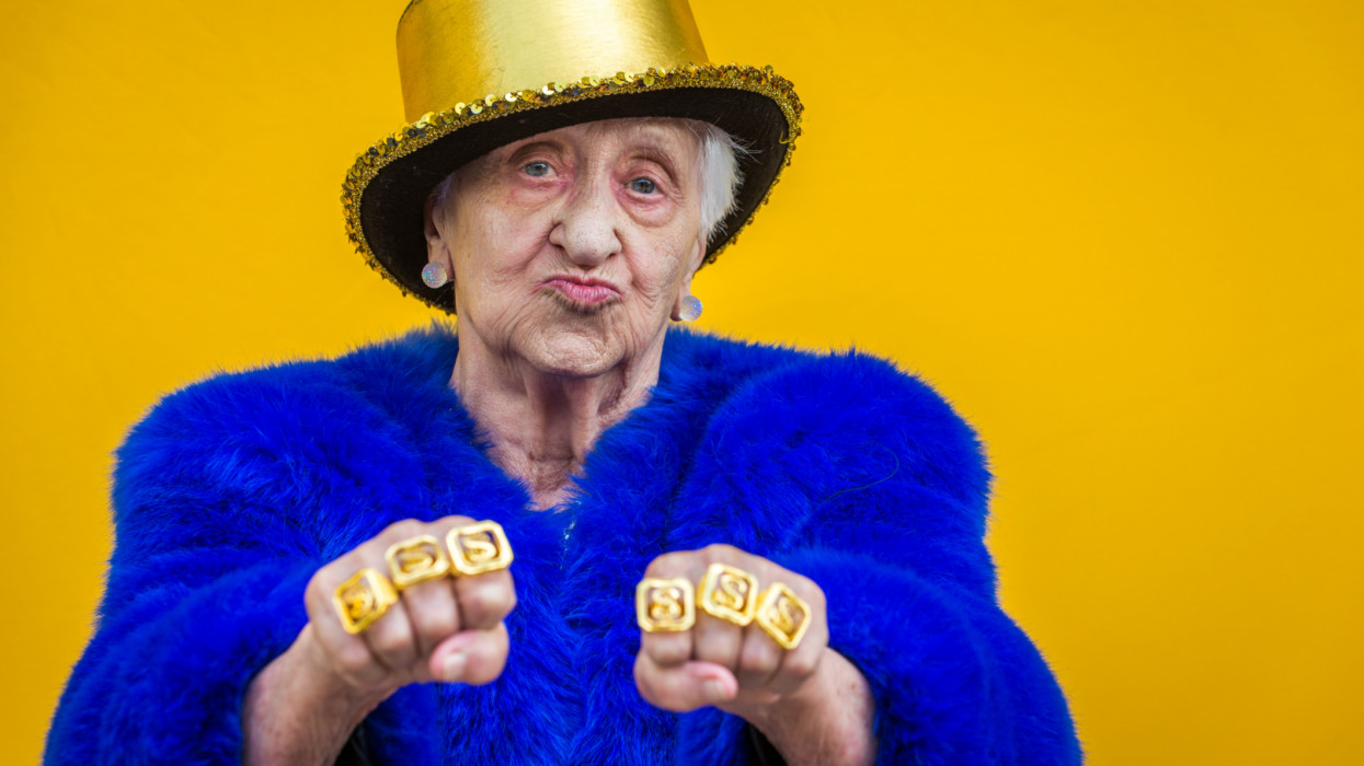 Funny and extravagant senior woman posing on colored background - Youthful old woman in the sixties having fun and partying