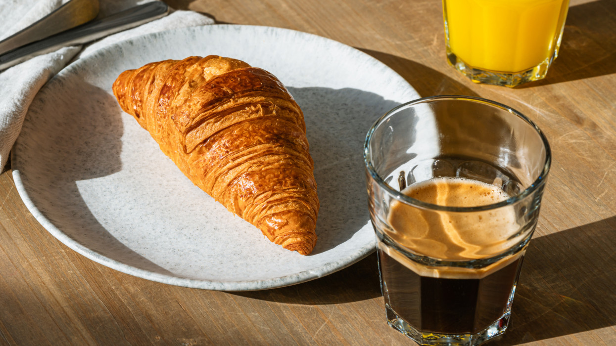 Breakfast with croissant, fresh coffee and orange juice on rustic wooden table. Sunlight with harsh shadows, delicious tasty morning meal