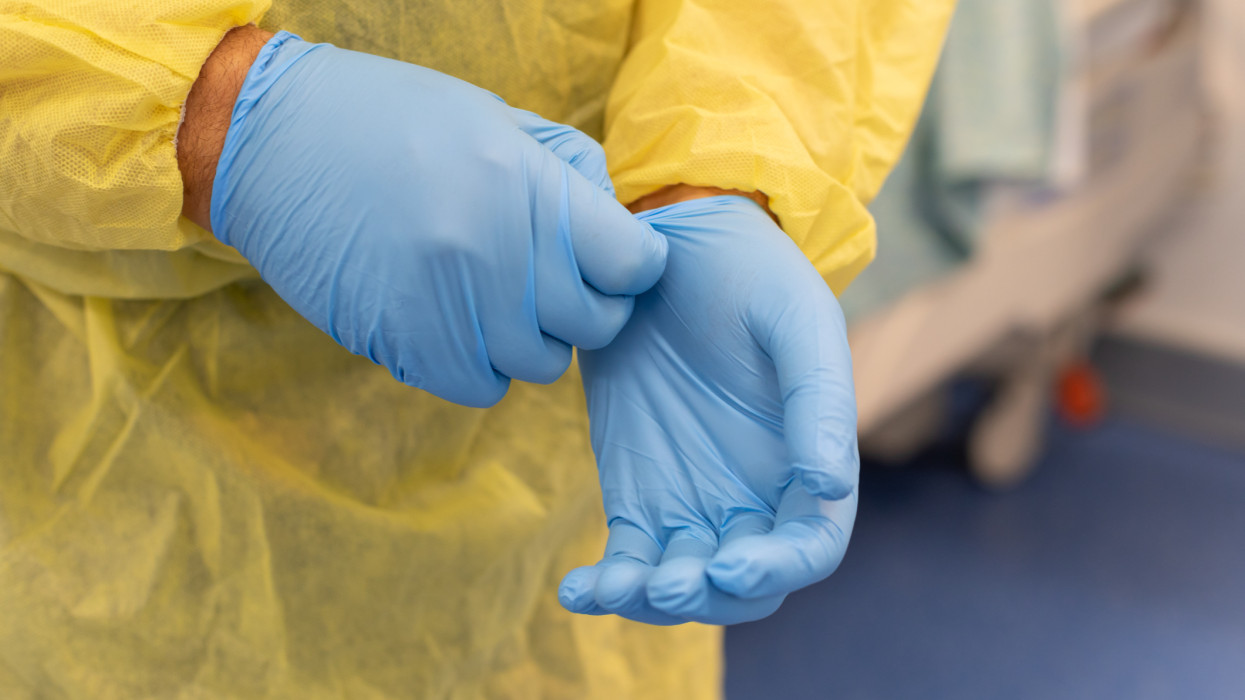 Showing Male hands removing blue healthcare gloves while wearing a protective gown, Australia