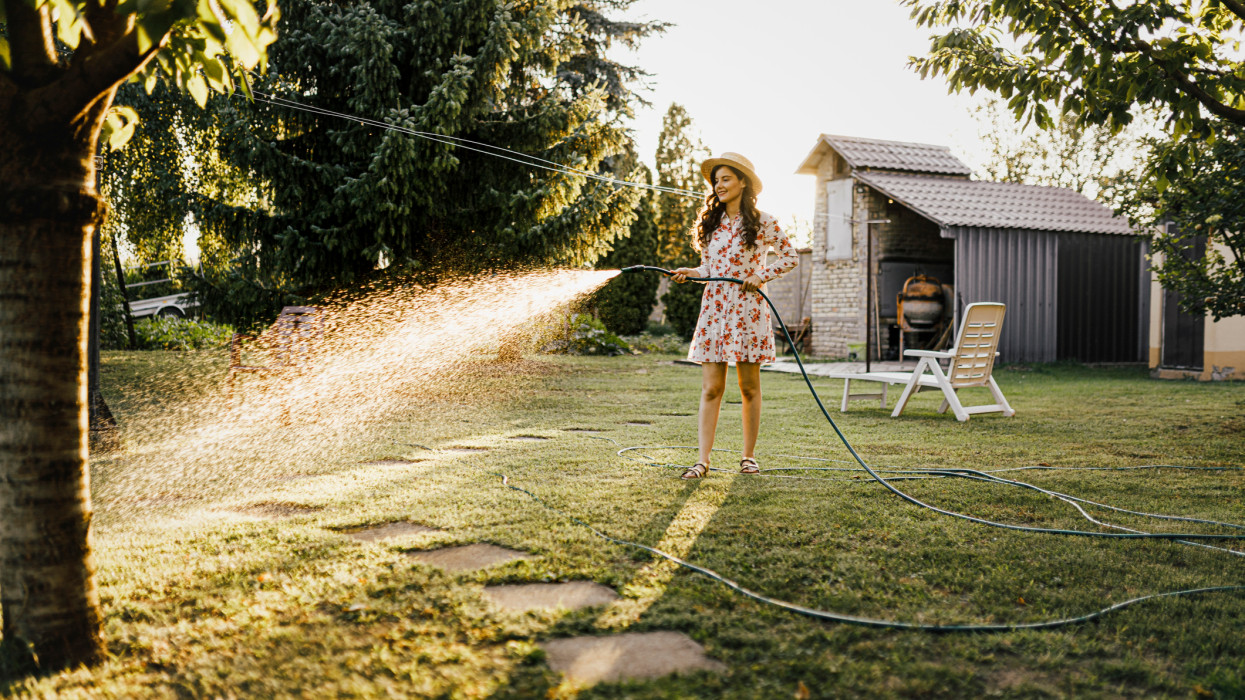 Shot of a woman watering plants with a garden hose in backyard