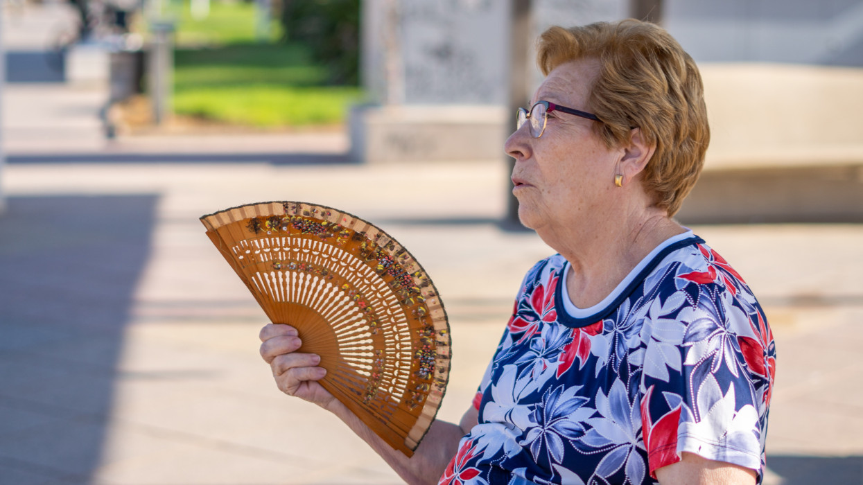 Close portrait, older woman fanning herself on a hot day, sitting on a bench in the city