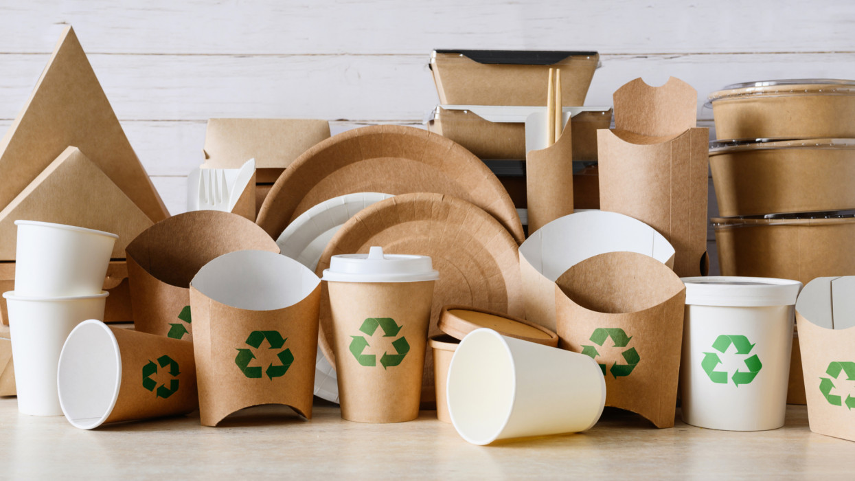 Containers and utensils for food made of biodegradable paper with a green recycling sign. The concept of recycling and zero waste