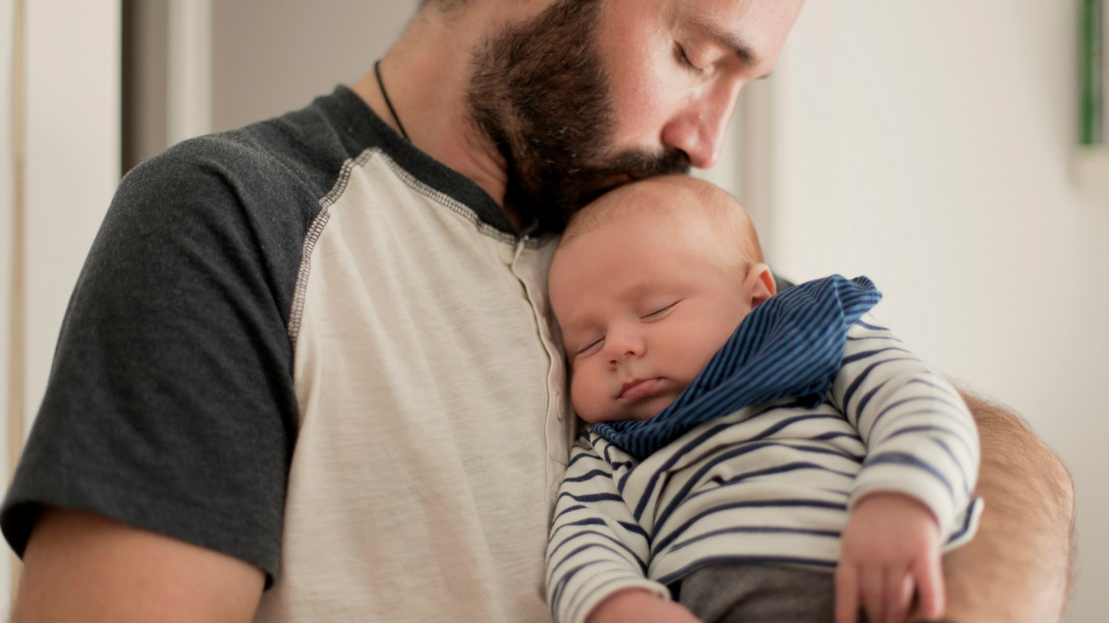 Apa megcsókolja újszülött gyermekét, aki elaludt a karjaiban.