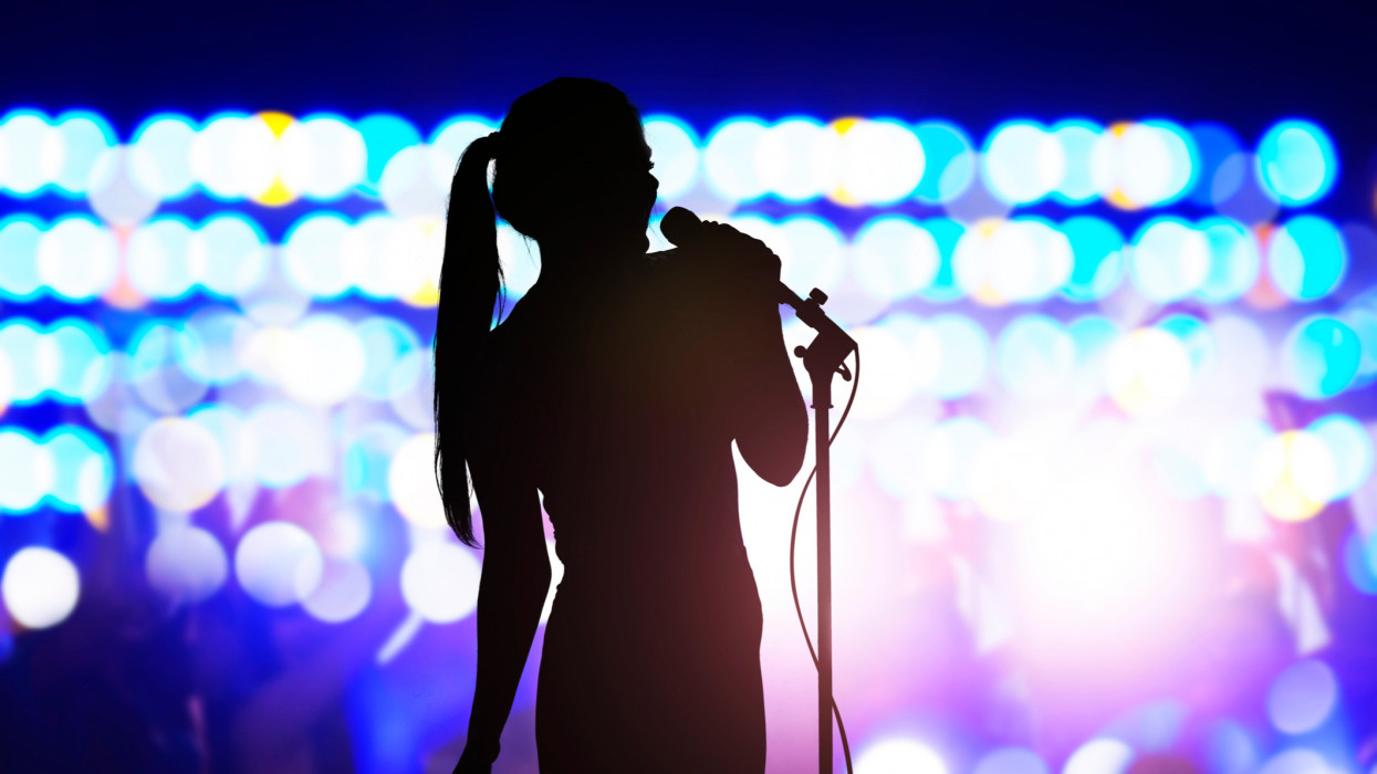Silhouette of woman with microphone singing on concert stage in front of crowd