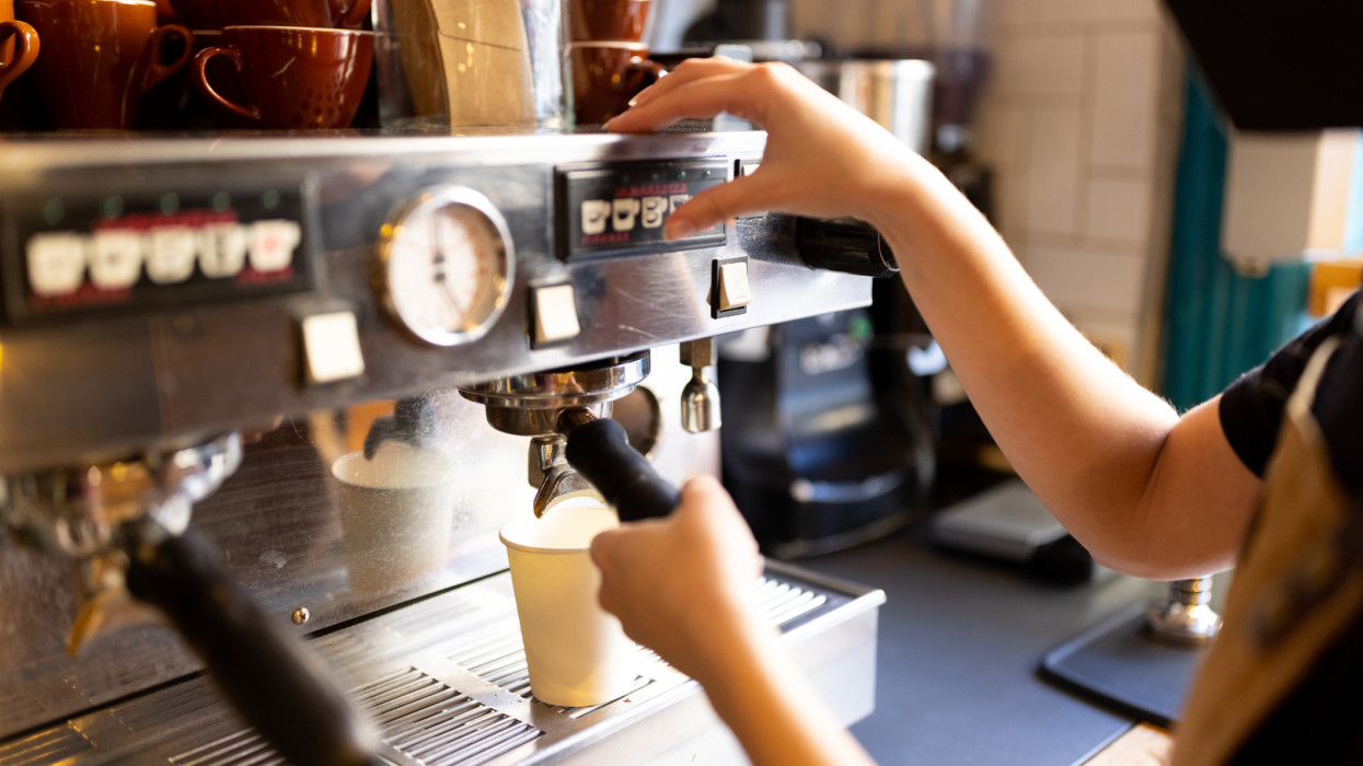 Young barista making a hot drink in a bakery using a coffee machine