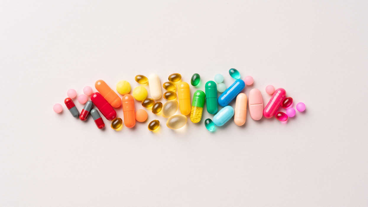 A Group of Multi Colored Medical Pills Organized in a Row Directly Above View on Beige Background.