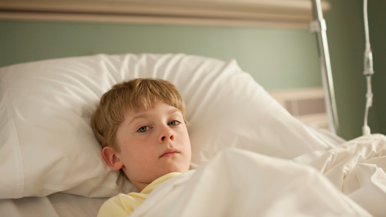 Young boy lying in hospital bed looking at camera with sad expression