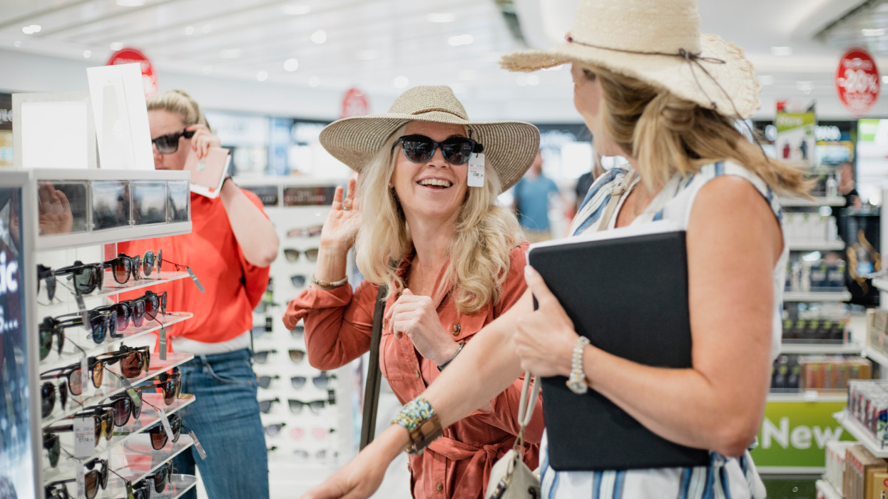 Mature woman are being playful while trying on sunglasses in Duty Free at the airport.