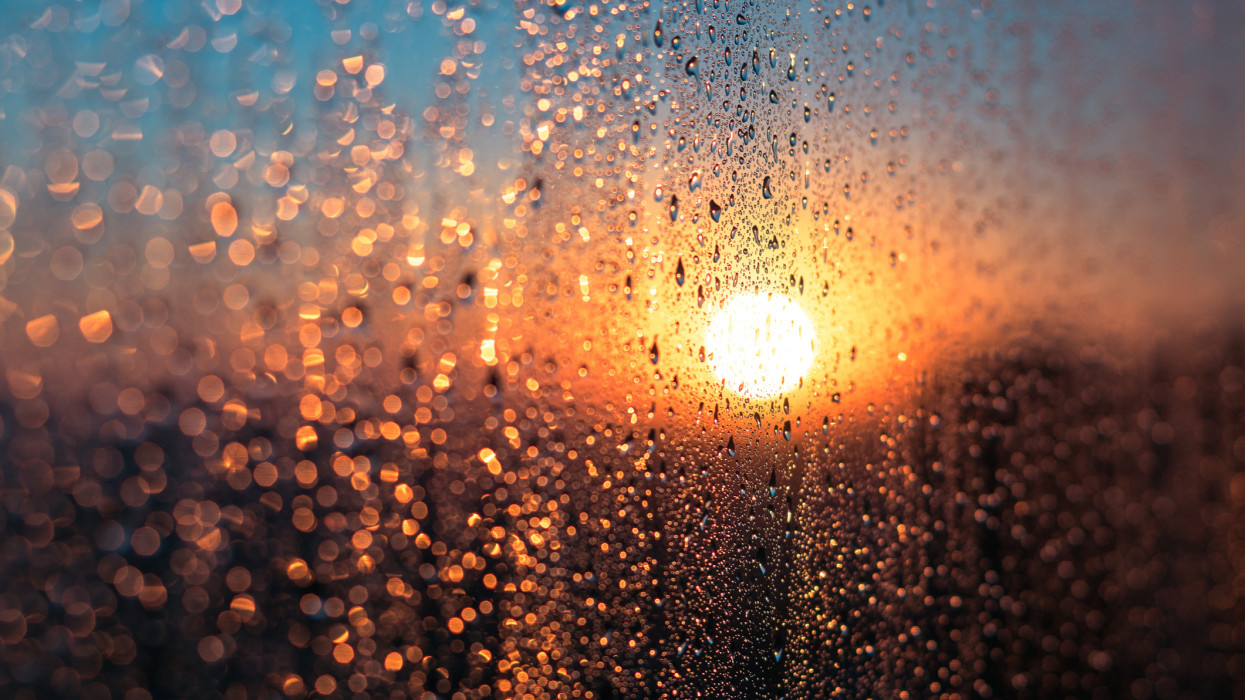 Wet Window with Condensation Water Against Sunrise or Sunset Glow in Cold Winter Day, Warm Indoor