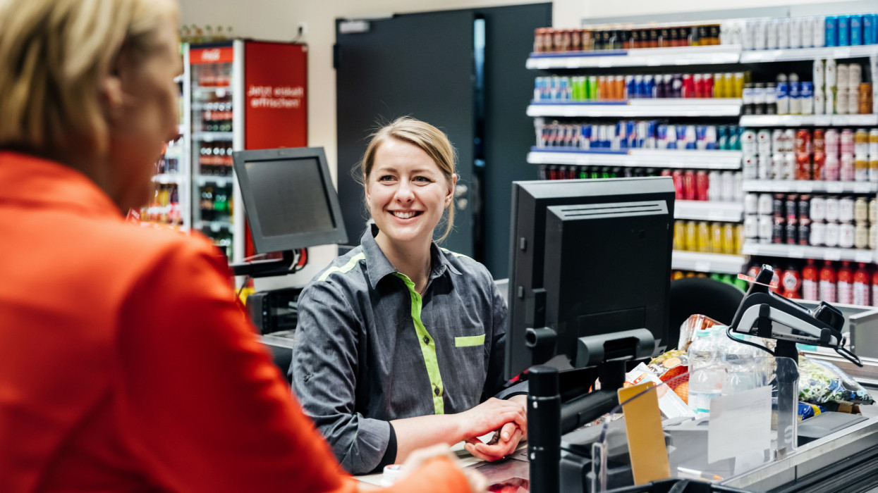 A cashier smiling at a customer who is buying groceries at her local supermarket.