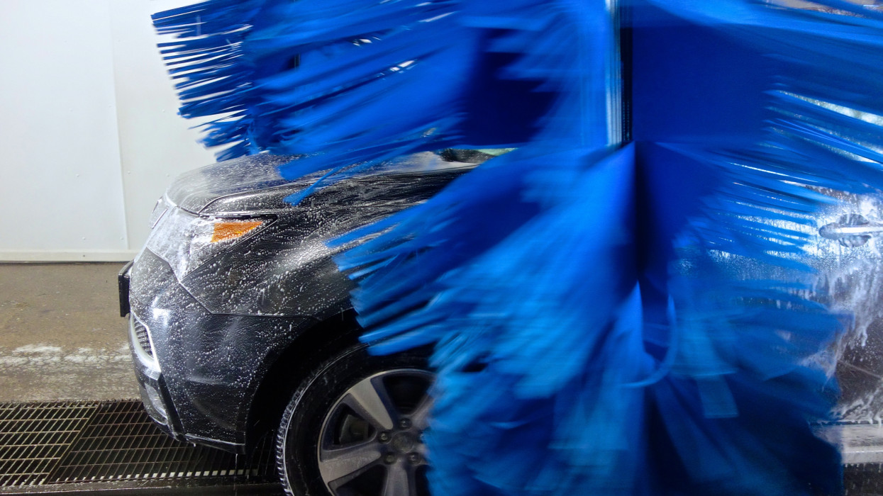 A side-profile of a soapy front-end of an SUV in an Automatic Carwash with Brushes spinning.