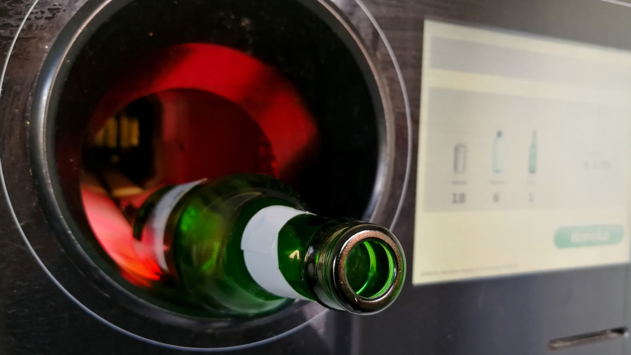 Green glass beer bottle close up inserted in the automatic reverse vending machine for recycling