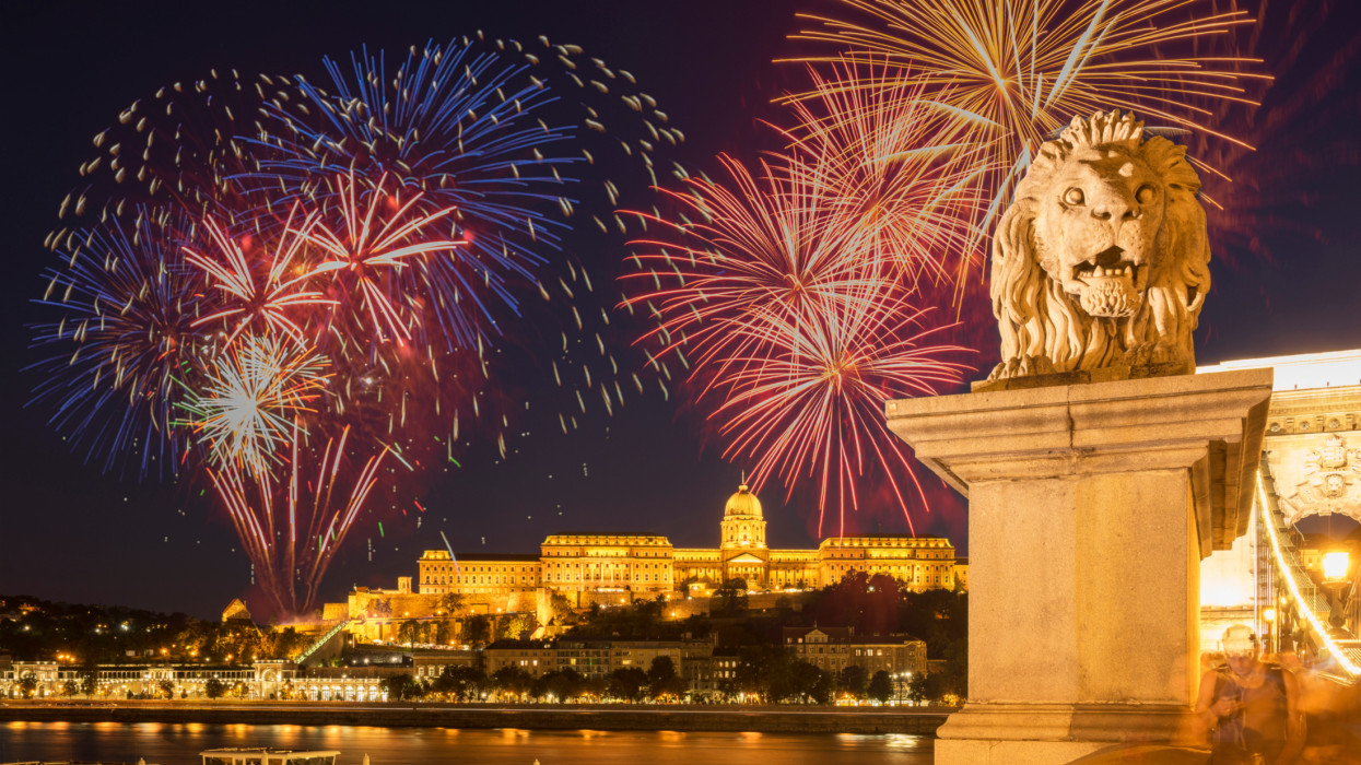 Hungary. Budapest. August 20th, 2022. View from the Danube bank of fireworks over the Buda Castle, the former Royal Palace of Budapest, Illuminated at night on the Hungary National Day. In foreground the lion statue hat the entrance of the famous Chain Bridge over the Danube.
