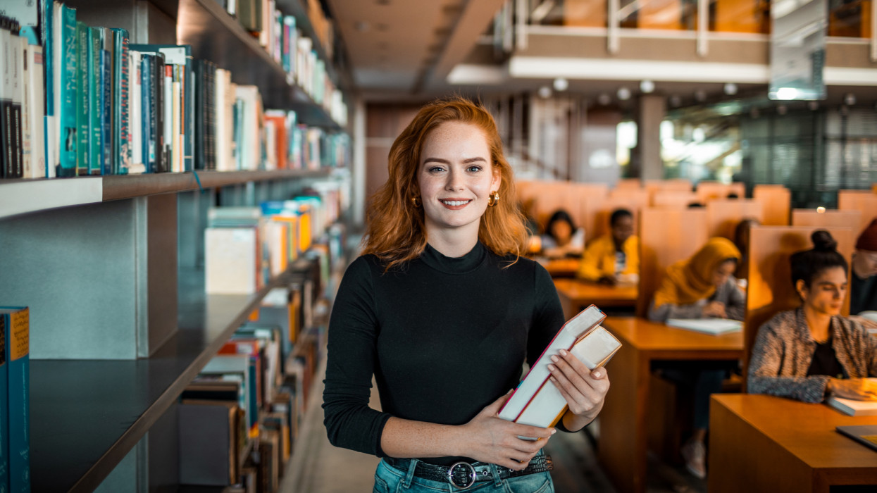 Close up portrait of a young woman holding a book in a library