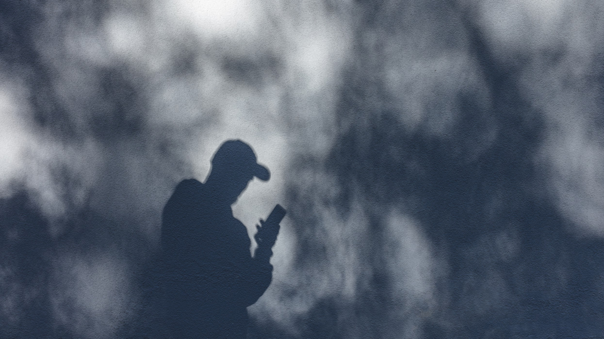 Man watching his phone against the plain wall with sunlight and shadows. Concept of technology and urban lifestyle in the city. Western Finland, Northern Europe