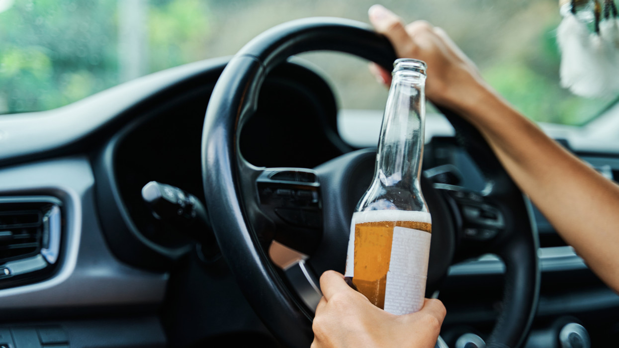 Young drunk woman drinking a beer while driving her car. Concept of alcohol abuse, addiction, alcoholism and dangerous driving.