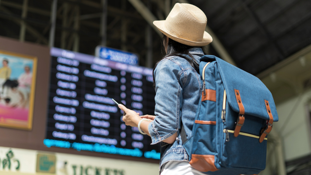 Backpacker young woman checking her train arrival in timetable board