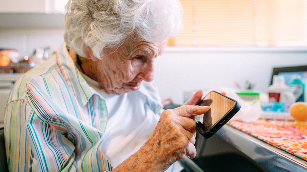 Elderly Senior Caucasian Woman Looking Closely and Using Her Index Finger to Digitally Sign her Electronic Signature on the Touch Screen of a Black Smart Phone Mobile Device for Online Contract Signing or Electronic Banking AgreementMobile Device Design has Been Modified in Post Production to be Non-Brand Specific.
