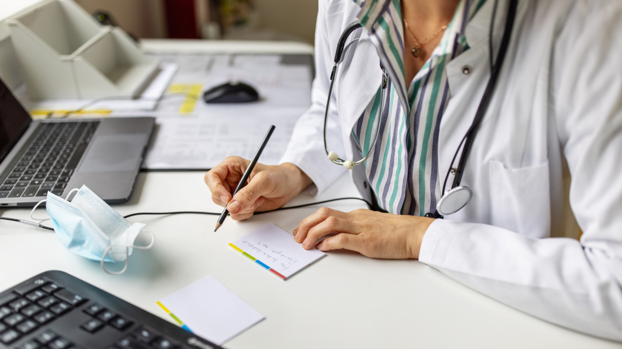 Close-up of a doctor preparing prescription while consulting a patient over video conference. Female doctor making notes while talking with patient on video call.
