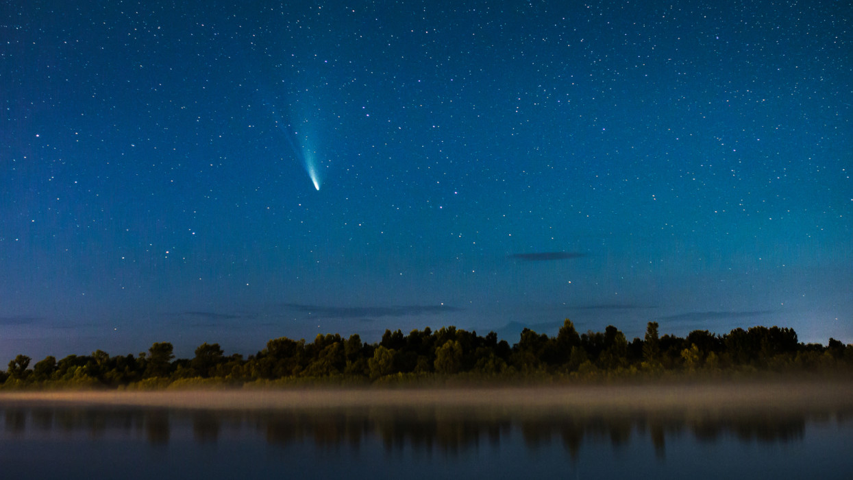 Comet in the night sky. Summer starry sky. Stars on sky. Beautiful night landscape. Long exposure. Conceptual photography. Fog over the water. Atmospheric landscape. Morning twilight. Comet Neowise