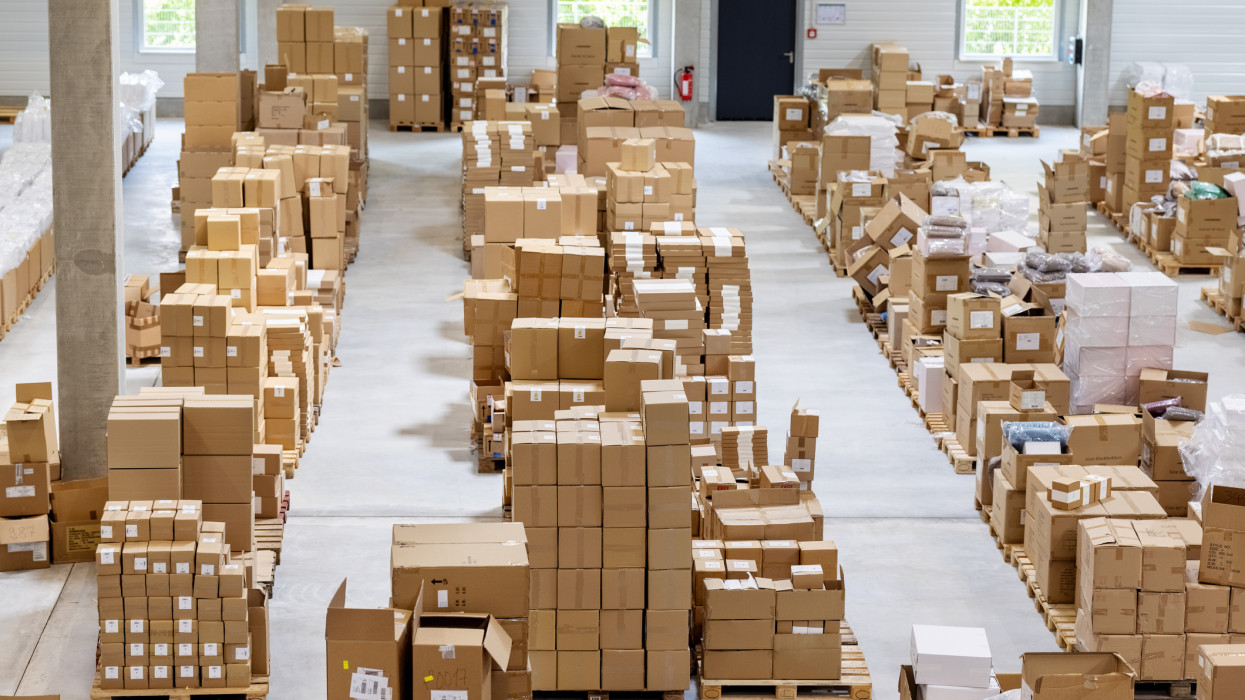 High angle view of large supply chain fulfilment center. Interior of a distribution warehouse with stack of cardboard boxes stored on pallets in a row.