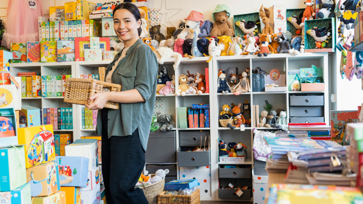 Wide view of young female Latin-American shop owner standing in her toy store