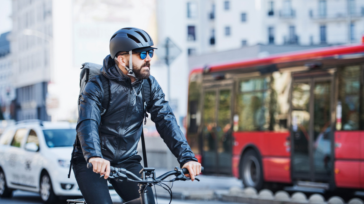 Férfi hipszter futár kerékpárral kerékpározik egy forgalmas városi úton, csomagokat kézbesítve. Másolási lehetőség.