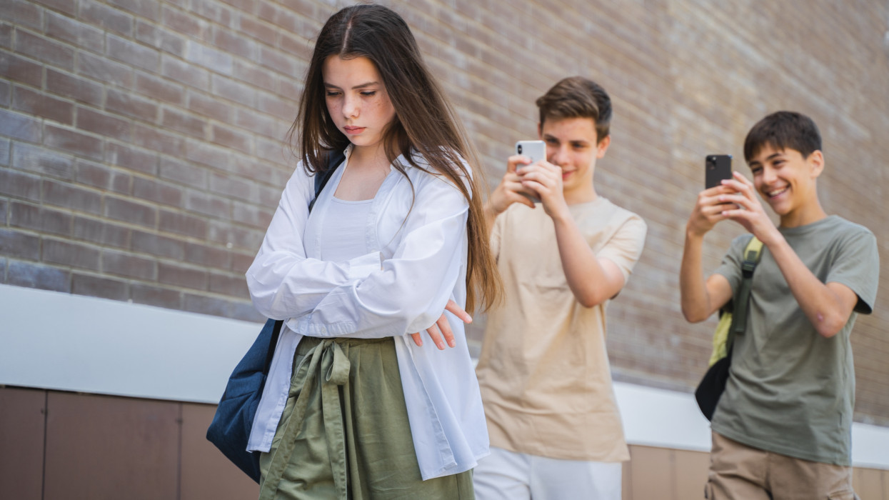 Two teenagers laugh at the girl and take a picture of her on the phone