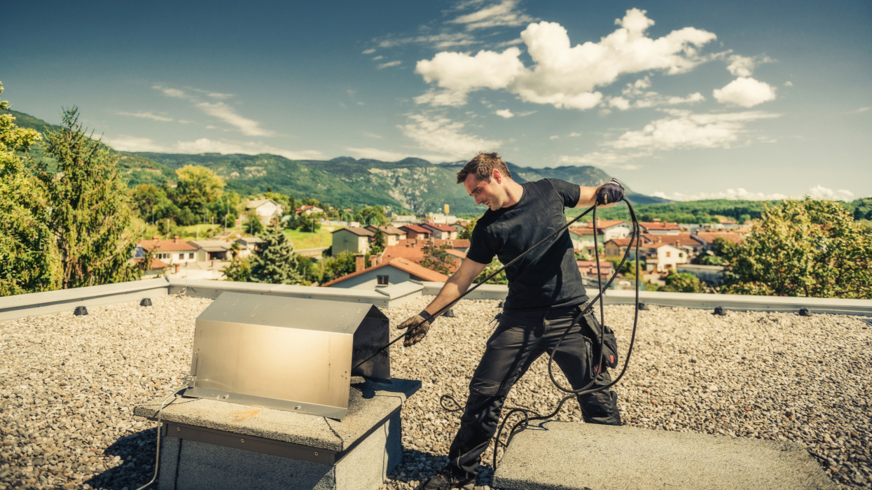 Chimney sweeper cleaning a chimney on top of the roof