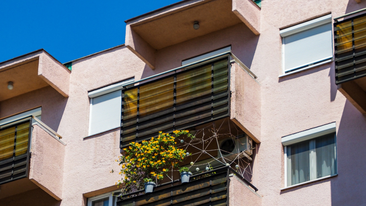 Detail closeup shot of a residential housing flat rental apartment building, blue sky pink wall windows balconies housing crisis Budapest, Hungary