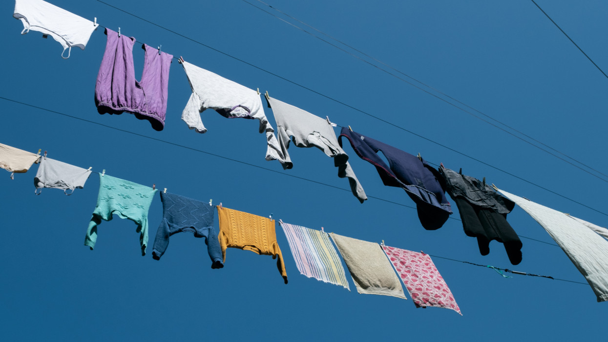 Clean sweaters, trousers and T-shirts hang on a rope outside on a sunny summer day, against a blue sky. Washed womens, mens and childrens clothes, bed linen are dried on a clothesline. The concept of housework, household duties.