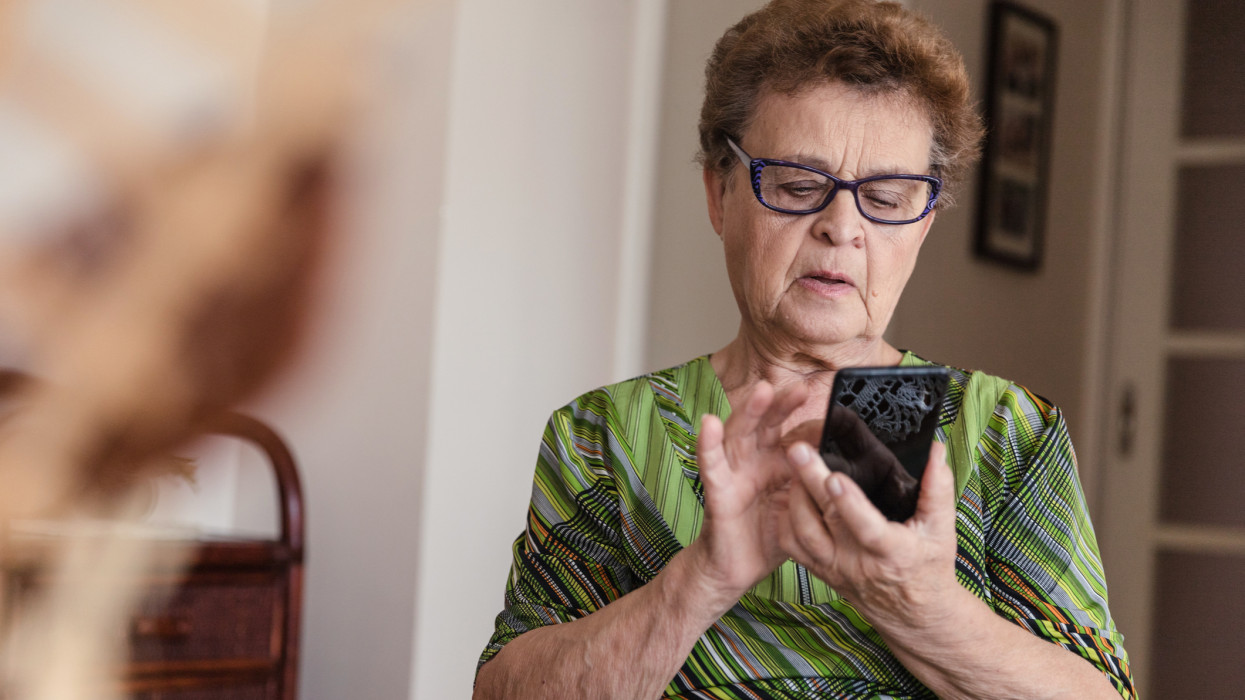 Senior woman sending a text message while sitting in her living room at home