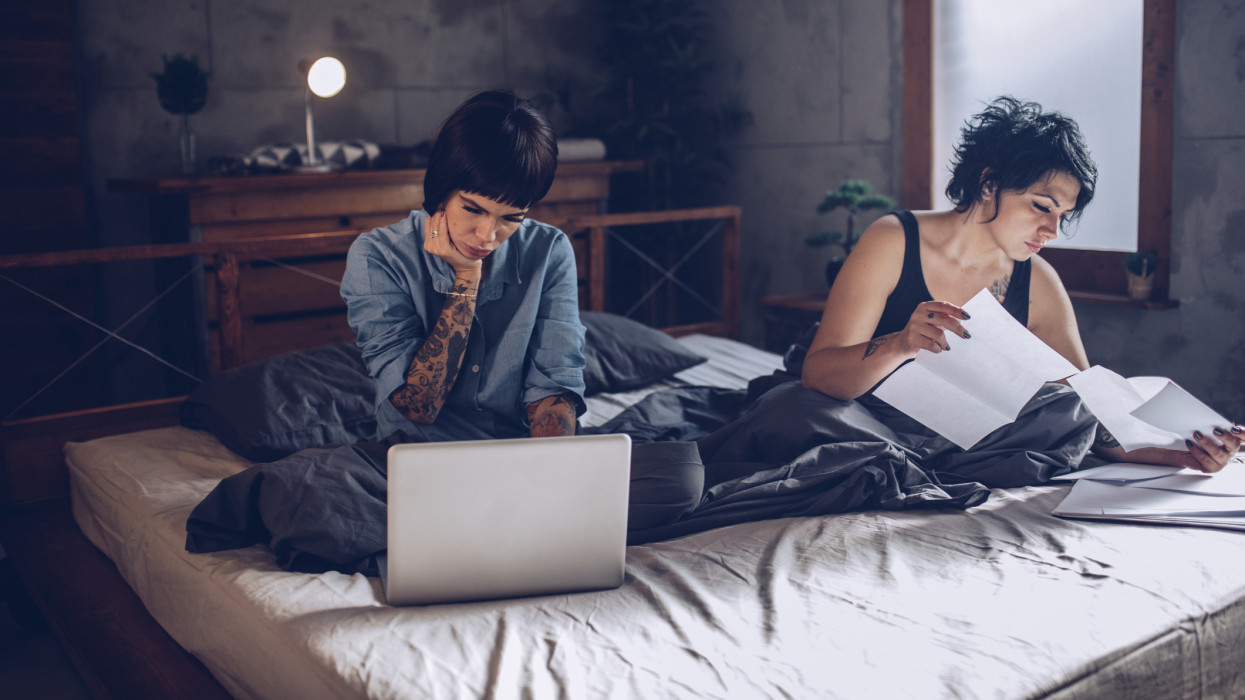 Two girls, young lesbian couple relaxing together at home in bed, looking sad, paying bills.