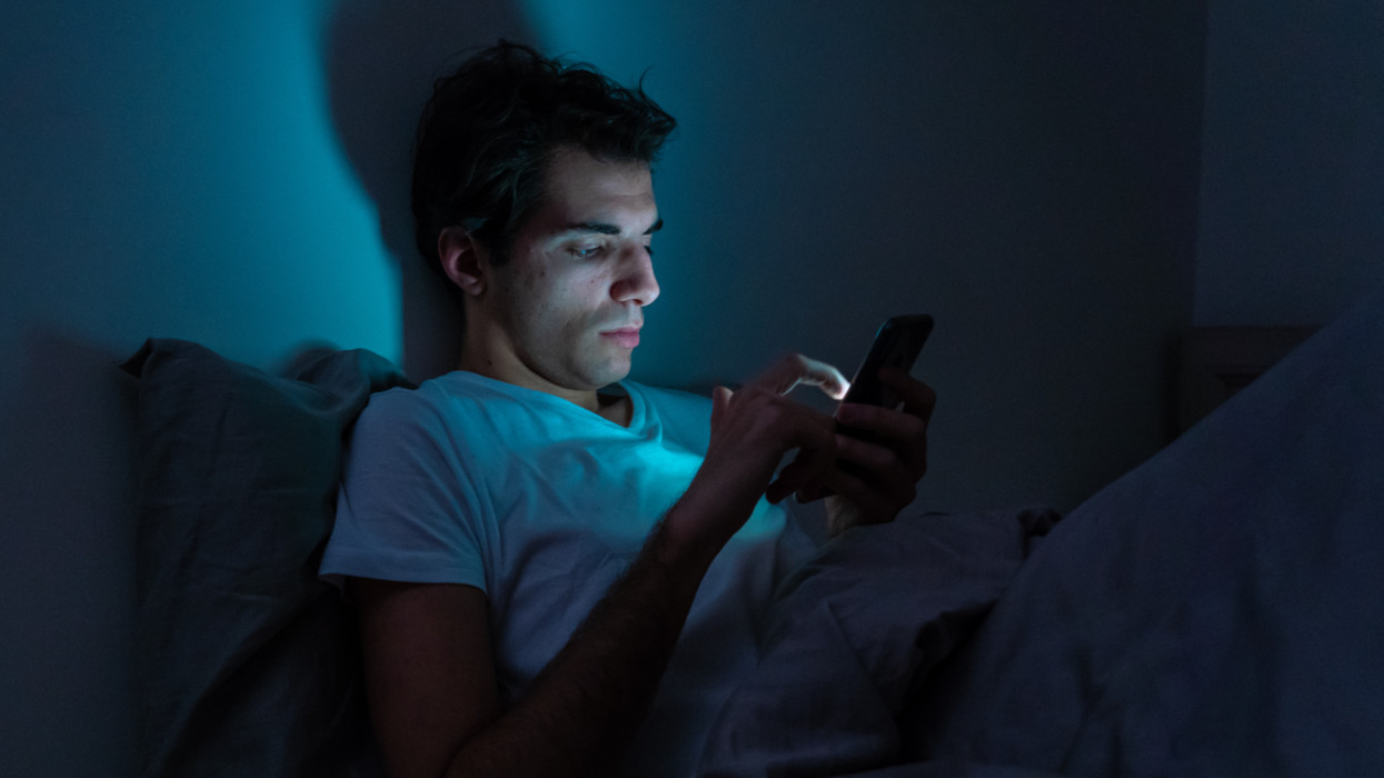 Lifestyle portrait of cell phone addict man awake late at night in bed using smart phone checking likes and followers, chatting, flirting, dating on social media. Internet addiction and mobile abuse.