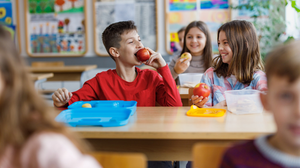 Smiling school kids enjoying on a break and eating apple