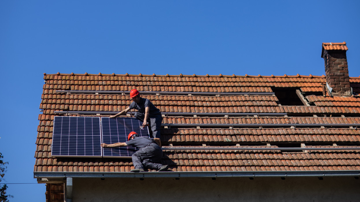Blue collar workers installing solar panels on roof of house