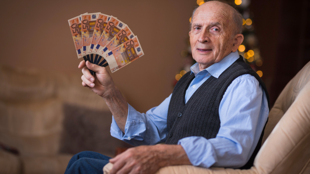 Cheerful grandfather sitting in a chair with a lot of money in his hand