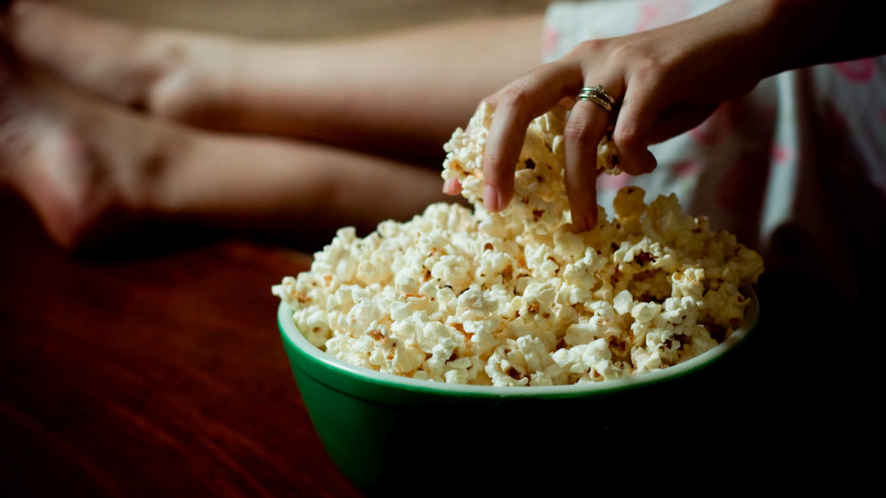 Woman hand into bowl filled with popcorn and her feet up on couch.