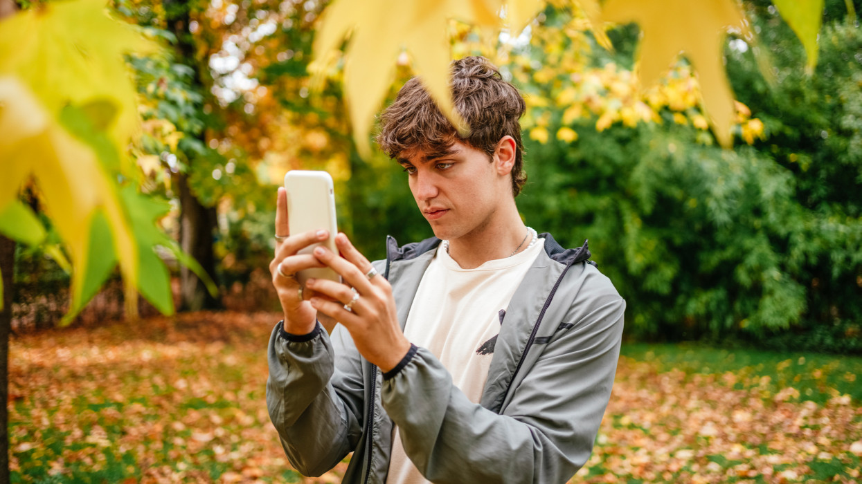 Portrait of a young man taking a selfie with his mobile phone among the leaves of a tree in autumn.