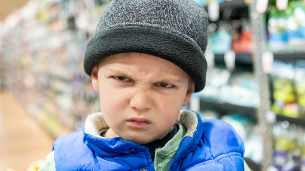 very upset three years old boy looking at the camera wearing a hat at the supermarket