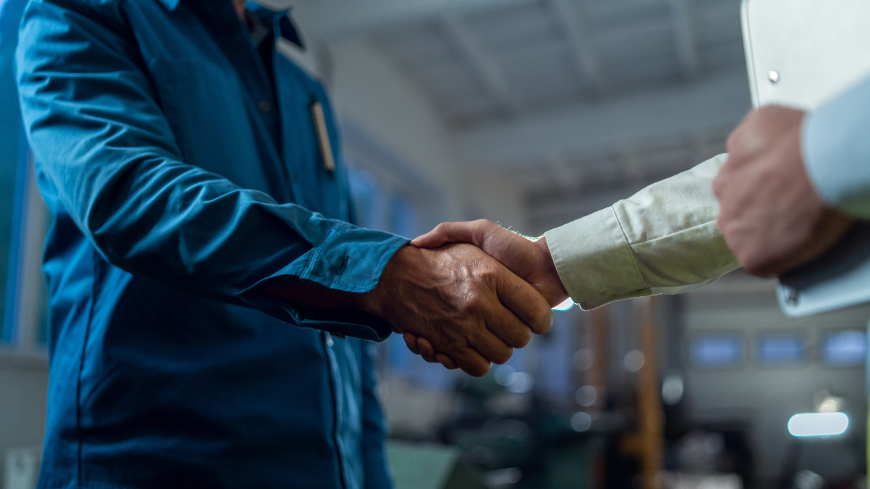 Japanese engineer shaking hands with mature worker indoors in metal workshop. Close-up.