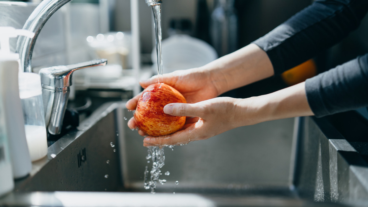 Cropped shot of womans hand washing an red apple with running water in the kitchen sink at home