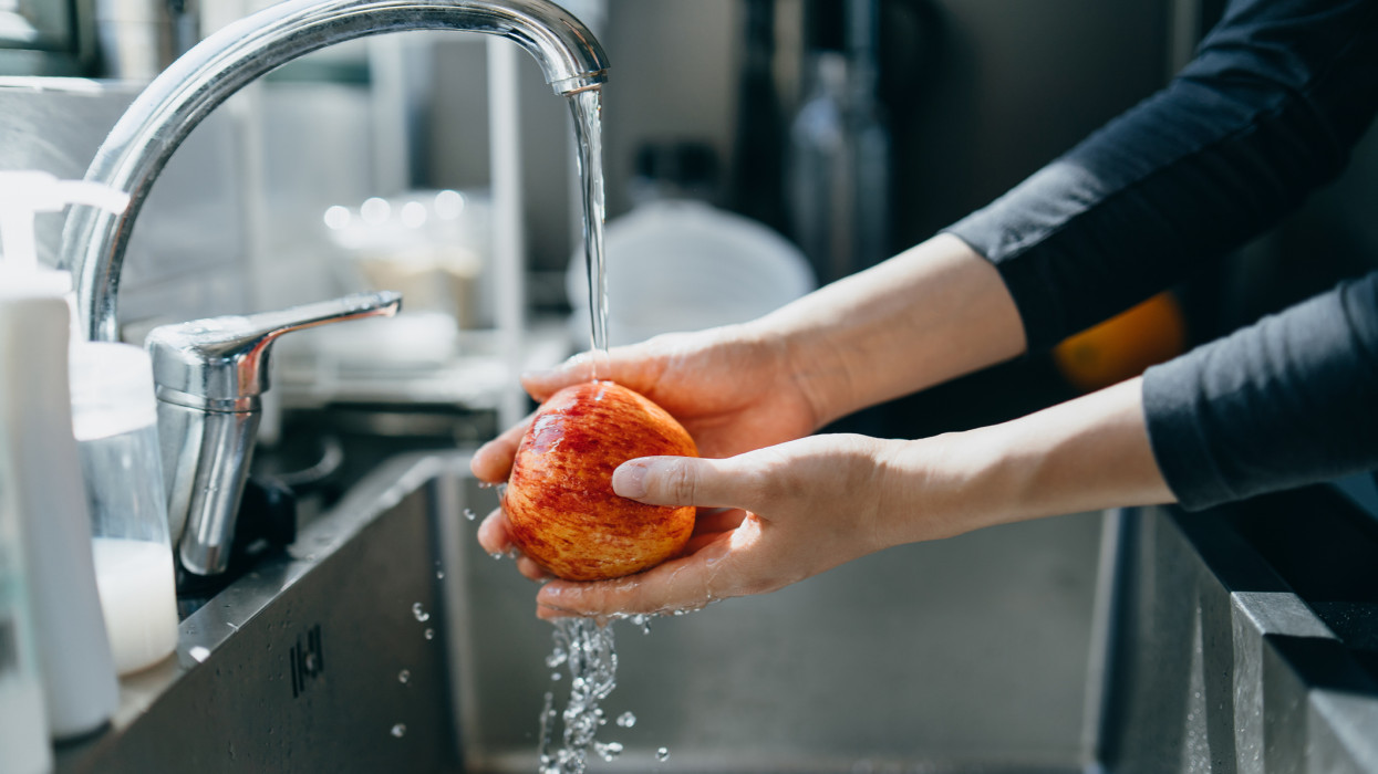 Cropped shot of womans hand washing an red apple with running water in the kitchen sink at home