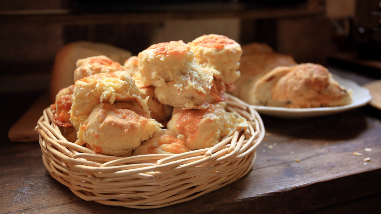 A basket of homemade cheese scones on a rustic wooden table.