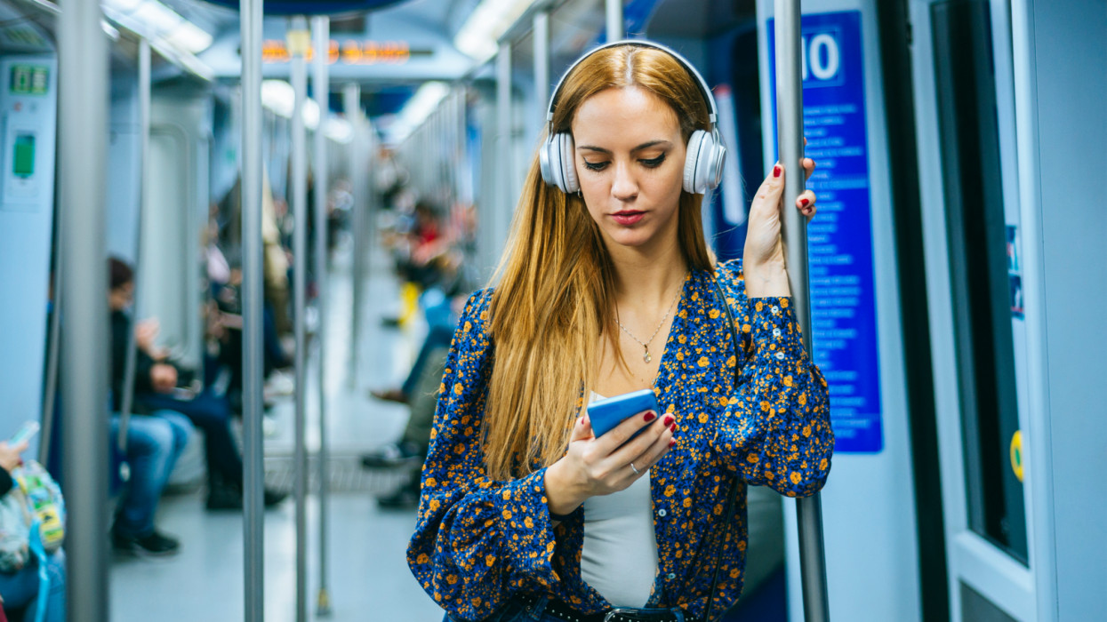 Woman with smartphone and headphones traveling in the subway music listening metro train