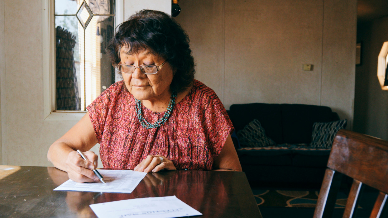 A senior aged Indigenous Navajo woman, preparing a mail in election ballot to vote.