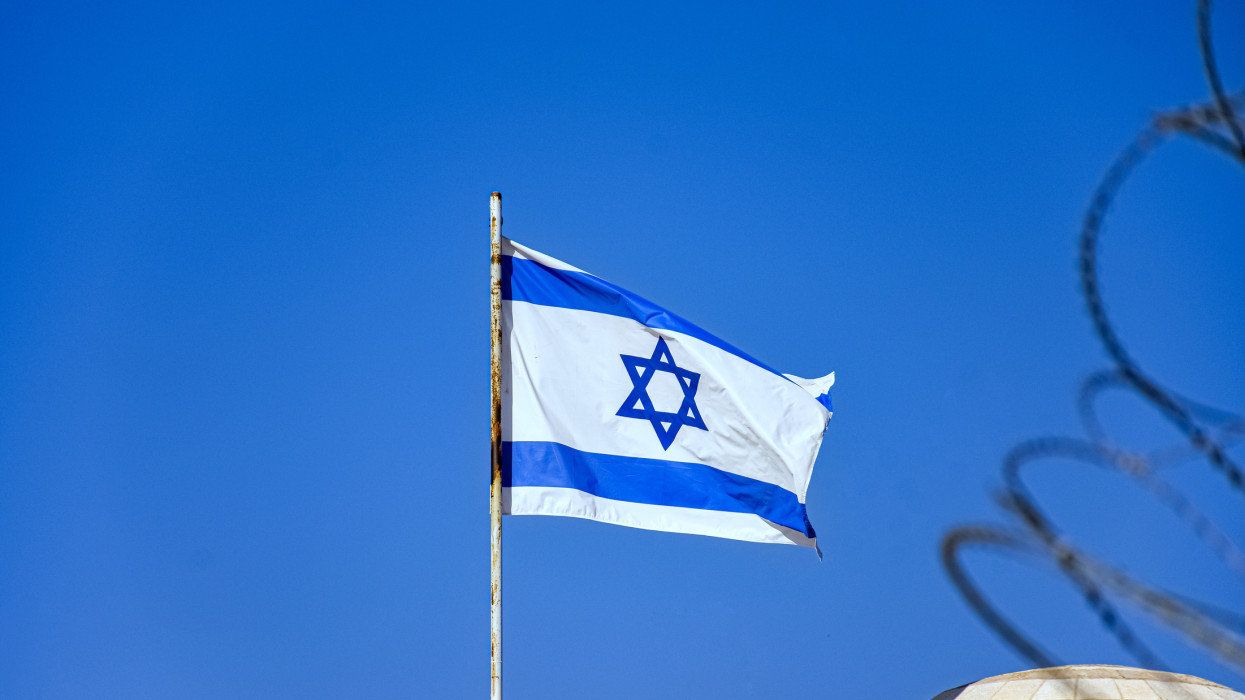 Israeli flag against clear blue sky and next to a barbed wire fence in old city of Jerusalem, Israel
